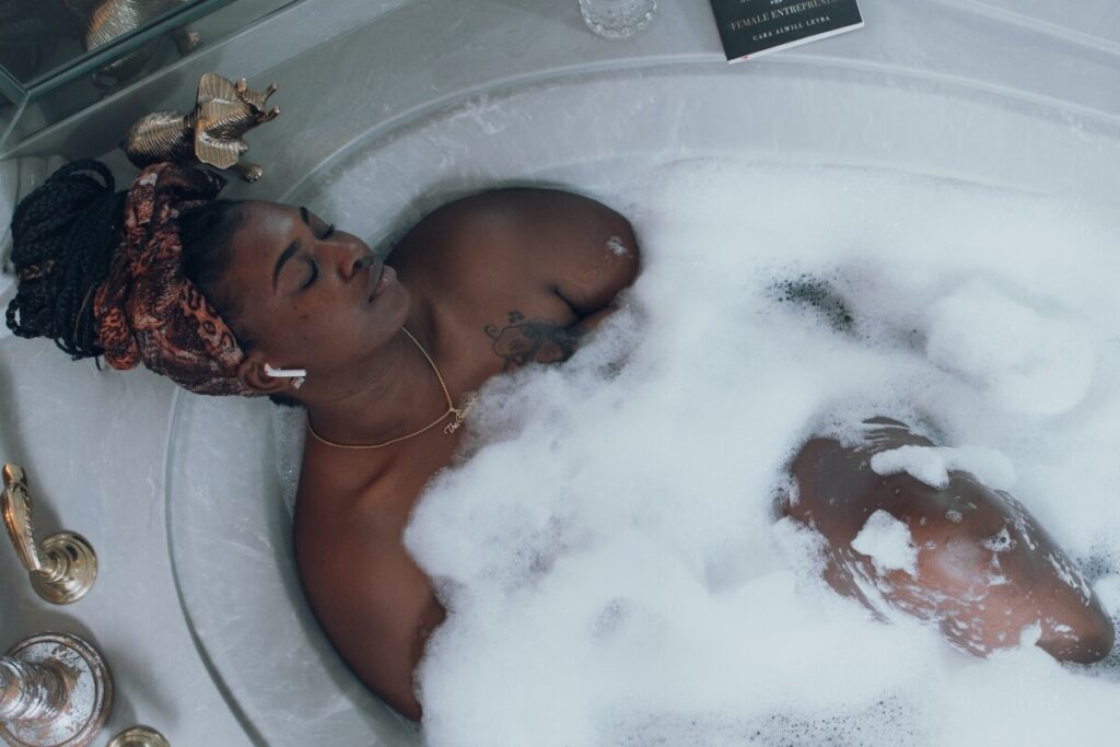 Image of a woman relaxing in a bubble bath, with a serene expression, highlighting a self-care ritual of taking a luxurious bath to relieve stress.
